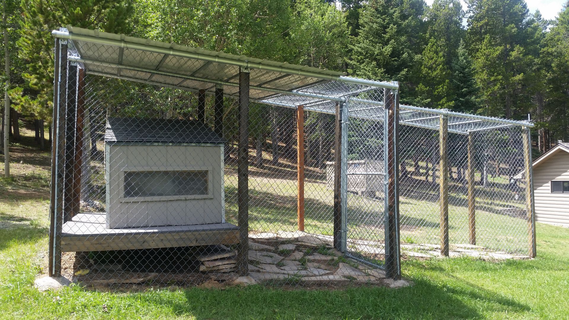 A chicken coop is surrounded by a chain link fence in a grassy field.
