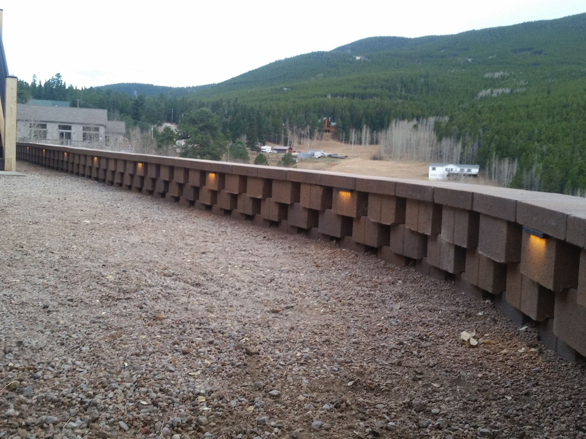 A brick wall with lights on it is surrounded by gravel and mountains in the background.