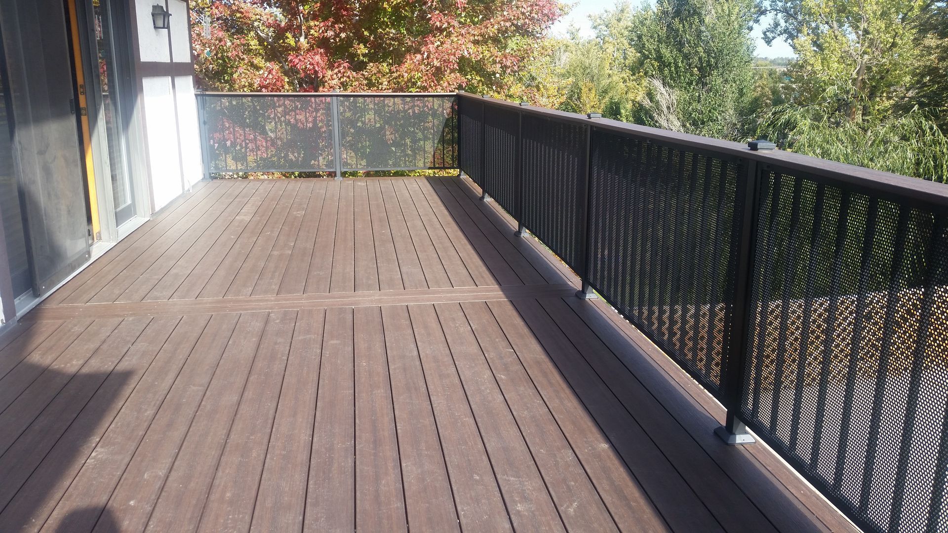 A wooden deck with a metal railing and trees in the background