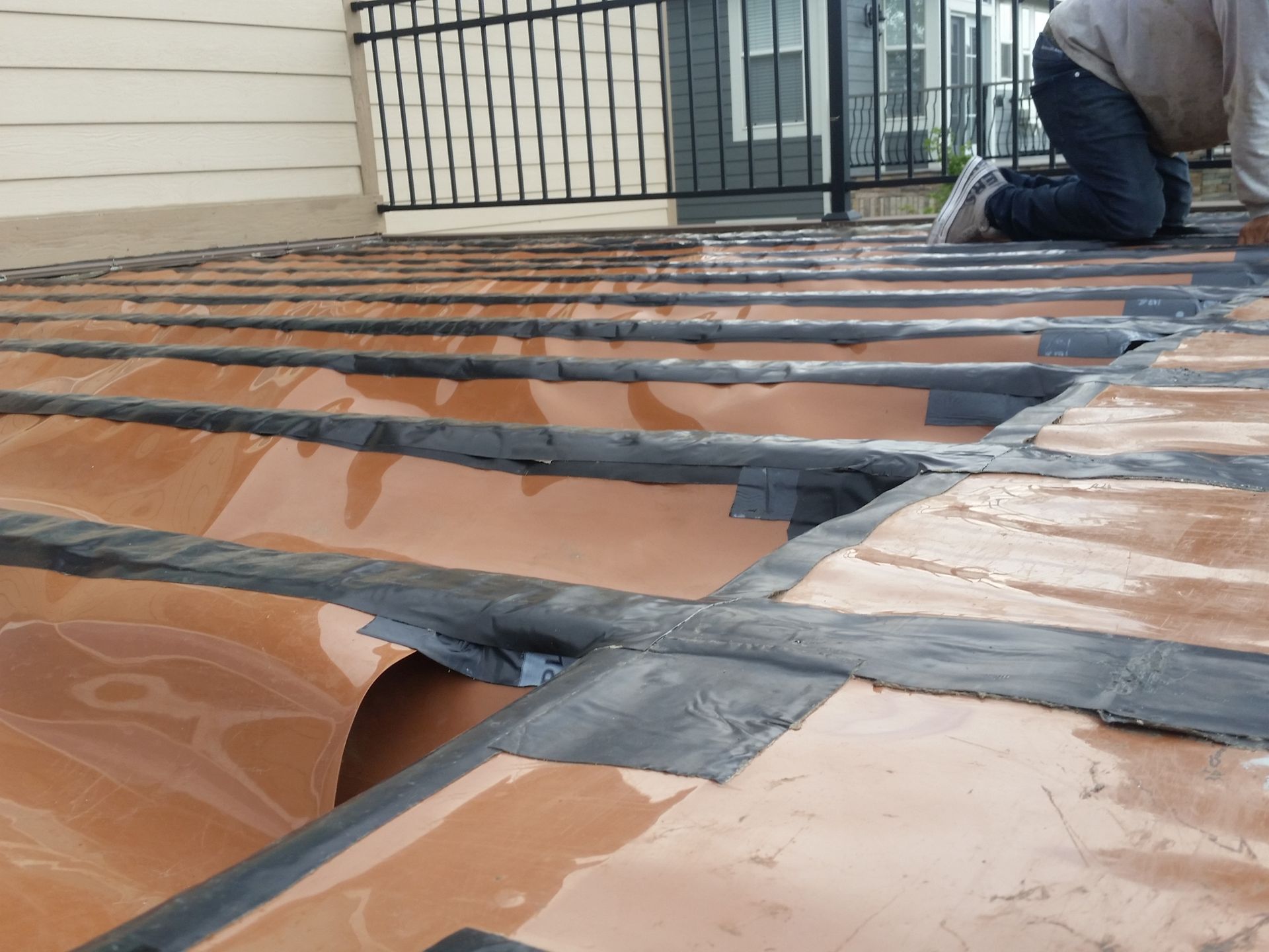 A man is kneeling on a roof with a fence in the background