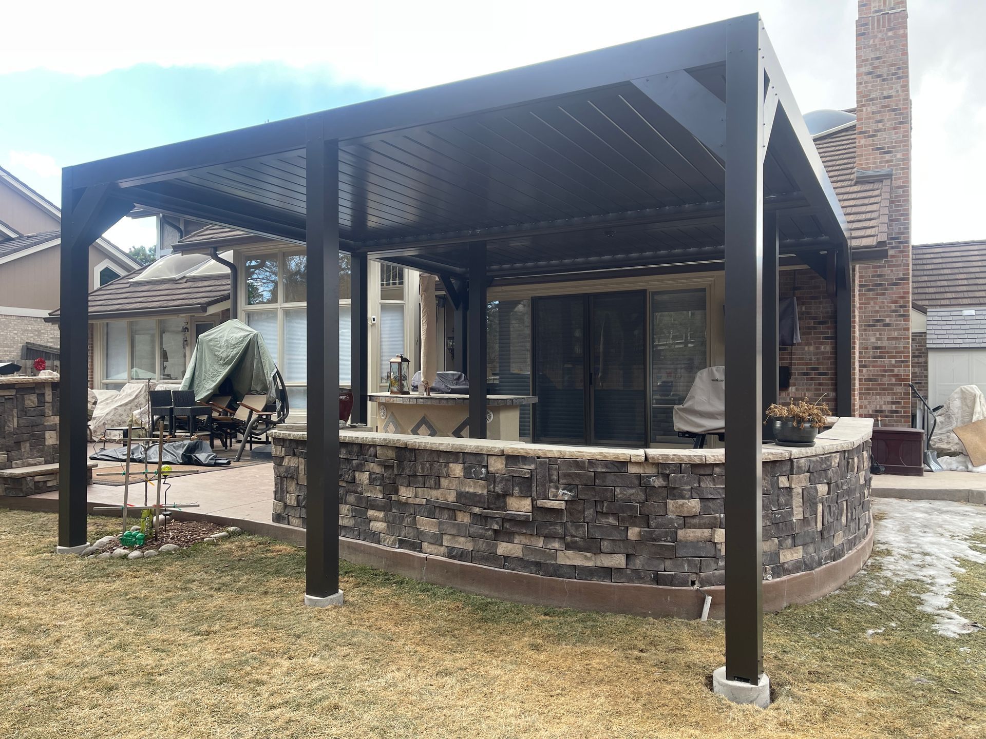 A Large black aluminum pergola covers the outdoor kitchen and porch of the home.
