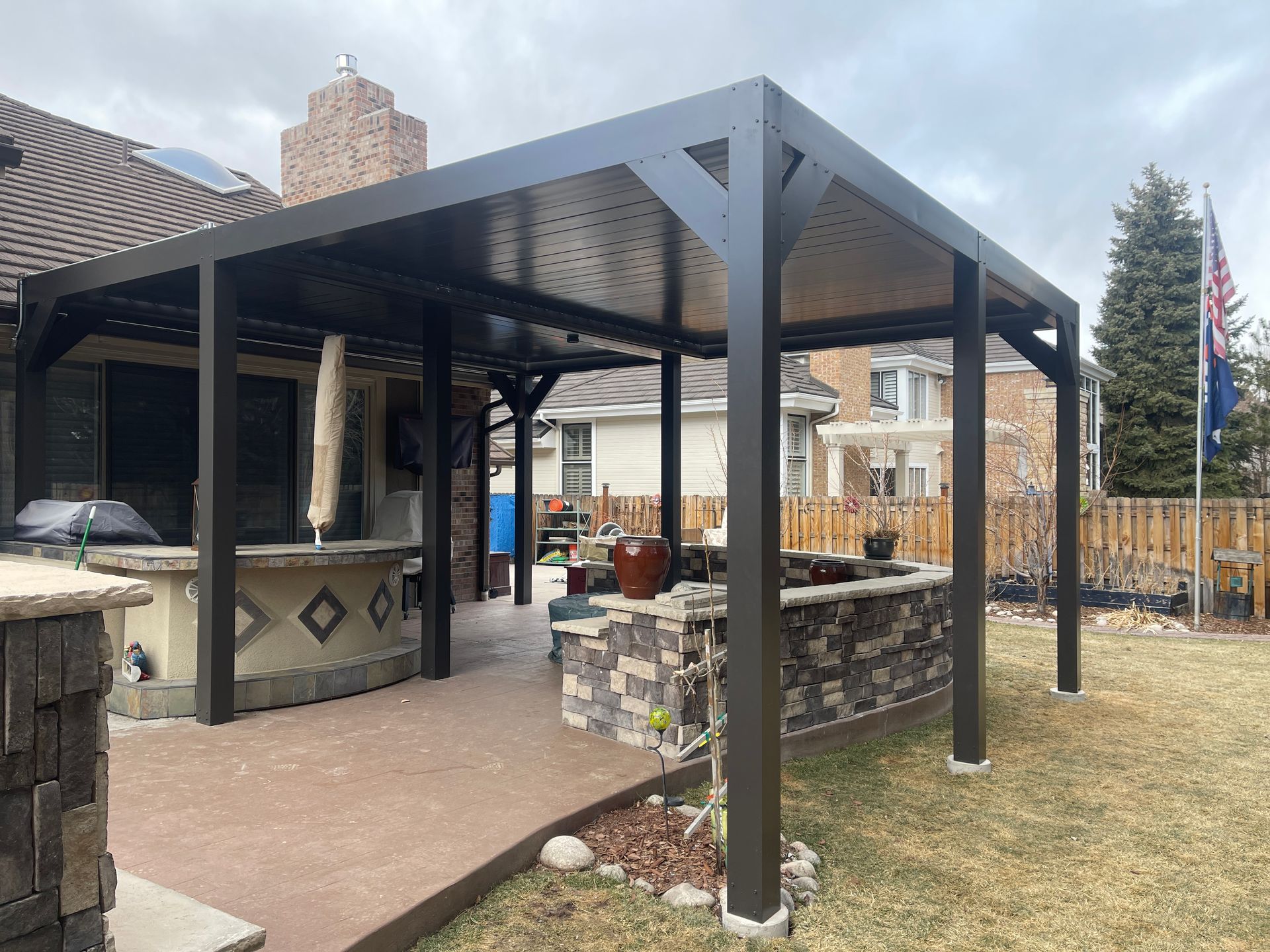 A patio with a pergola and a kitchen in the backyard of a house.