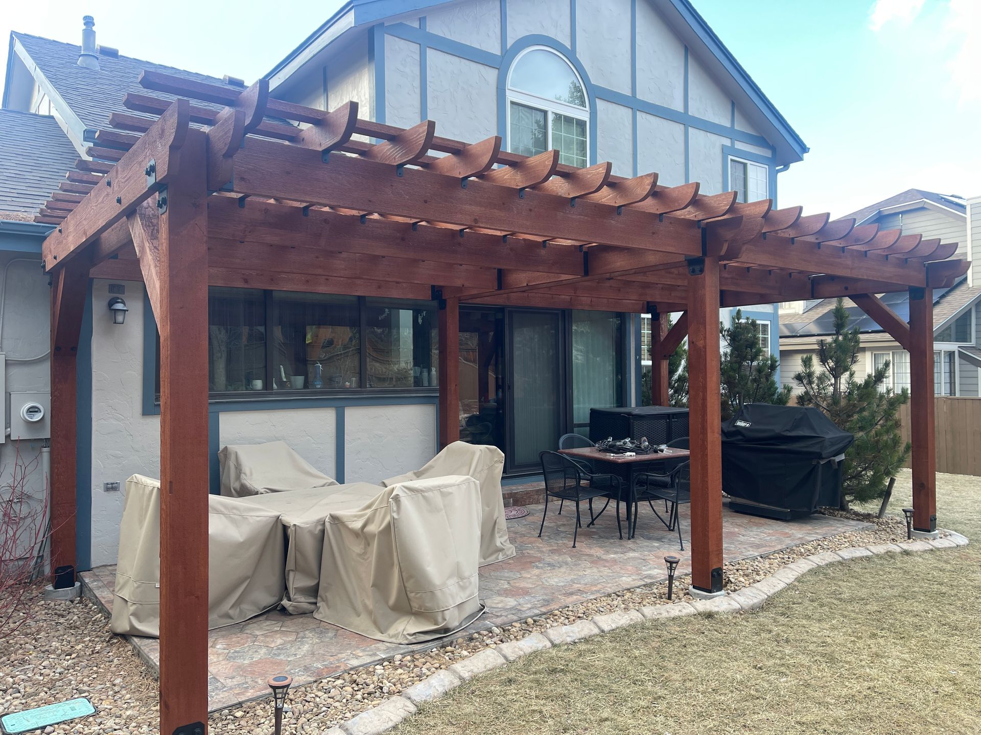 A wooden pergola is sitting in the backyard of a house.