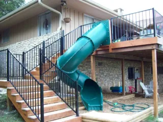Custom wooden deck with turquoise spiral slide and black metal railings featuring integrated playground equipment for family outdoor living