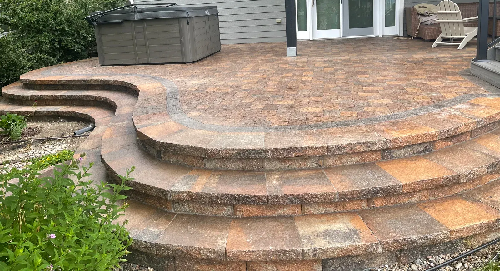 Brick patio with curved steps, leading to a hot tub. Steps are multi-toned brown.
