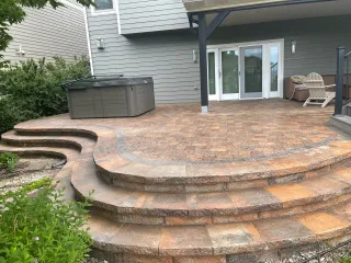 A paver patio with a curved multi-step staircase with a hot tub and some patio furniture.