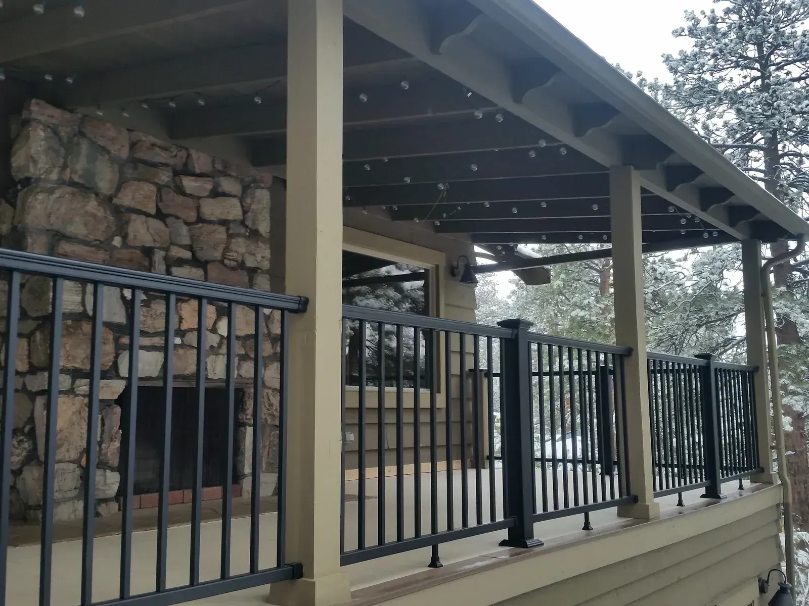 A porch with a roof and a black aluminum metal railing and a brick fireplace.