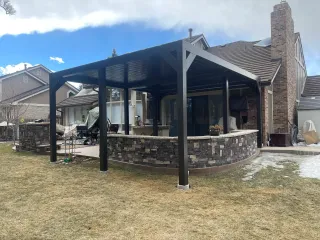 Modern covered outdoor kitchen with aluminum pergola and natural stone base featuring built-in appliances and seating area