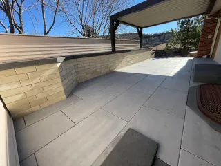 Modern multi-level patio with large format tile flooring, natural stone retaining walls, and aluminum pergola overlooking mountain views