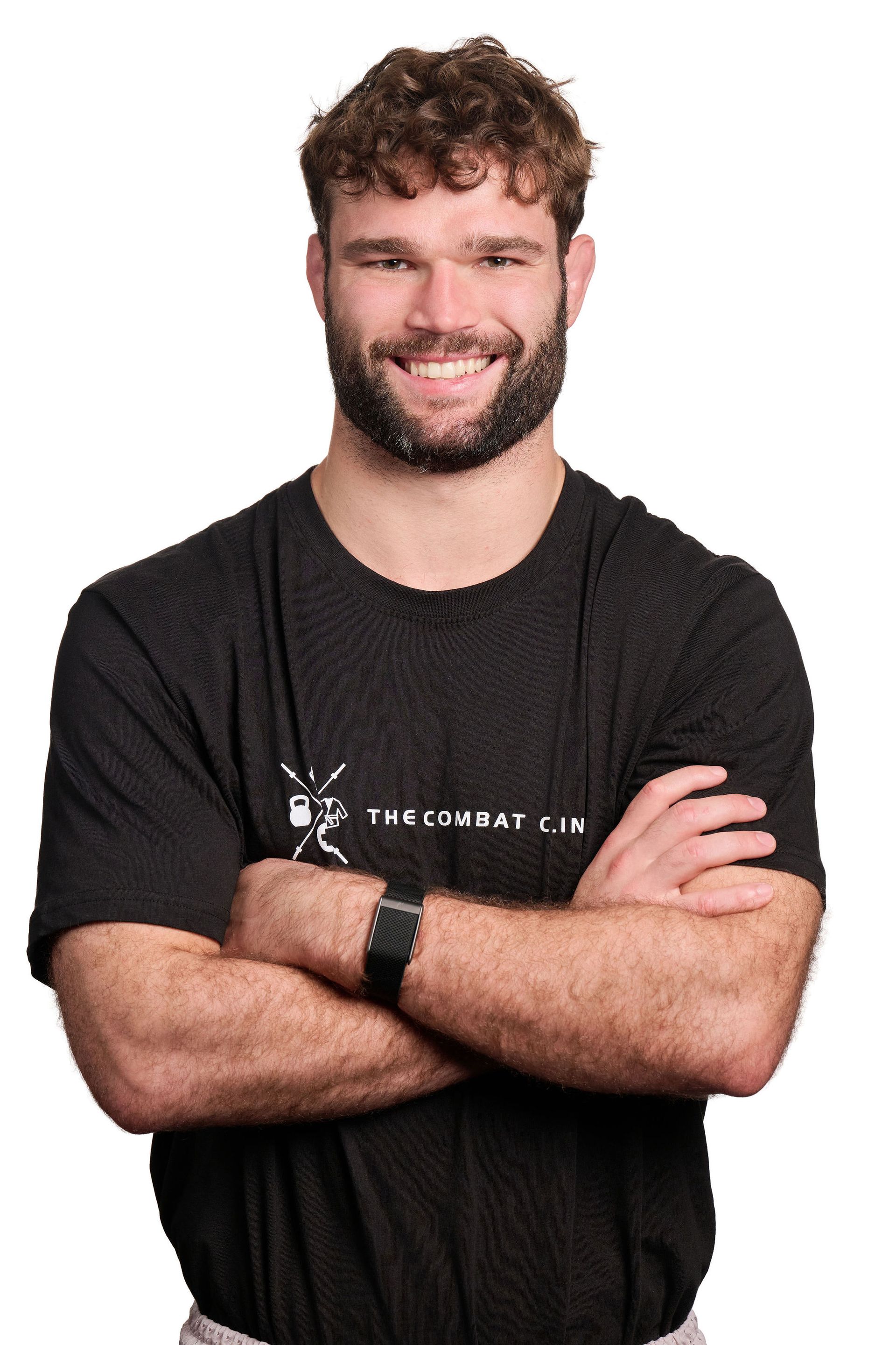 Man with arms crossed smiles in a gym. Sign for