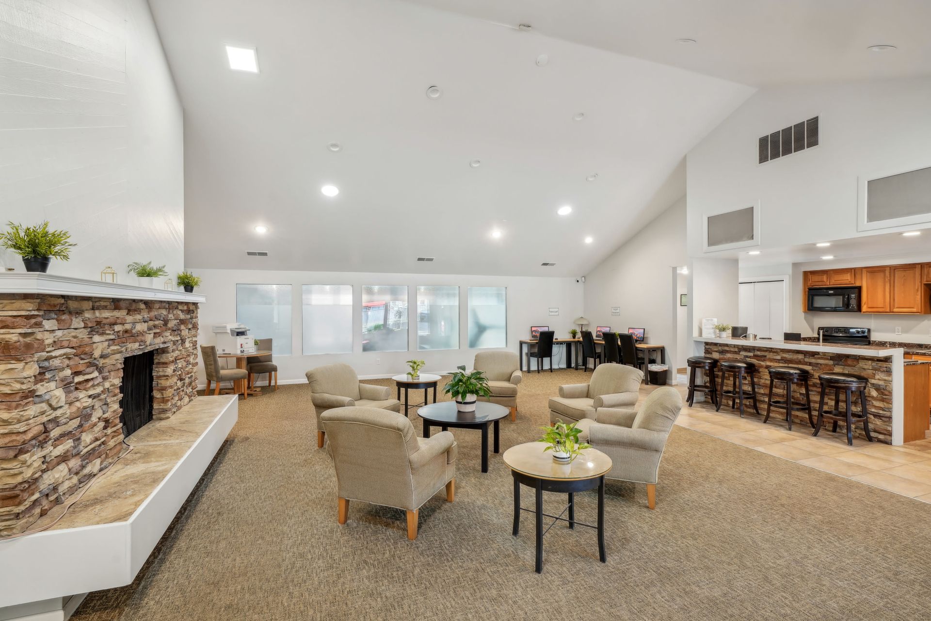 Spacious resident lounge with beige armchairs, circular tables, and a stone fireplace.