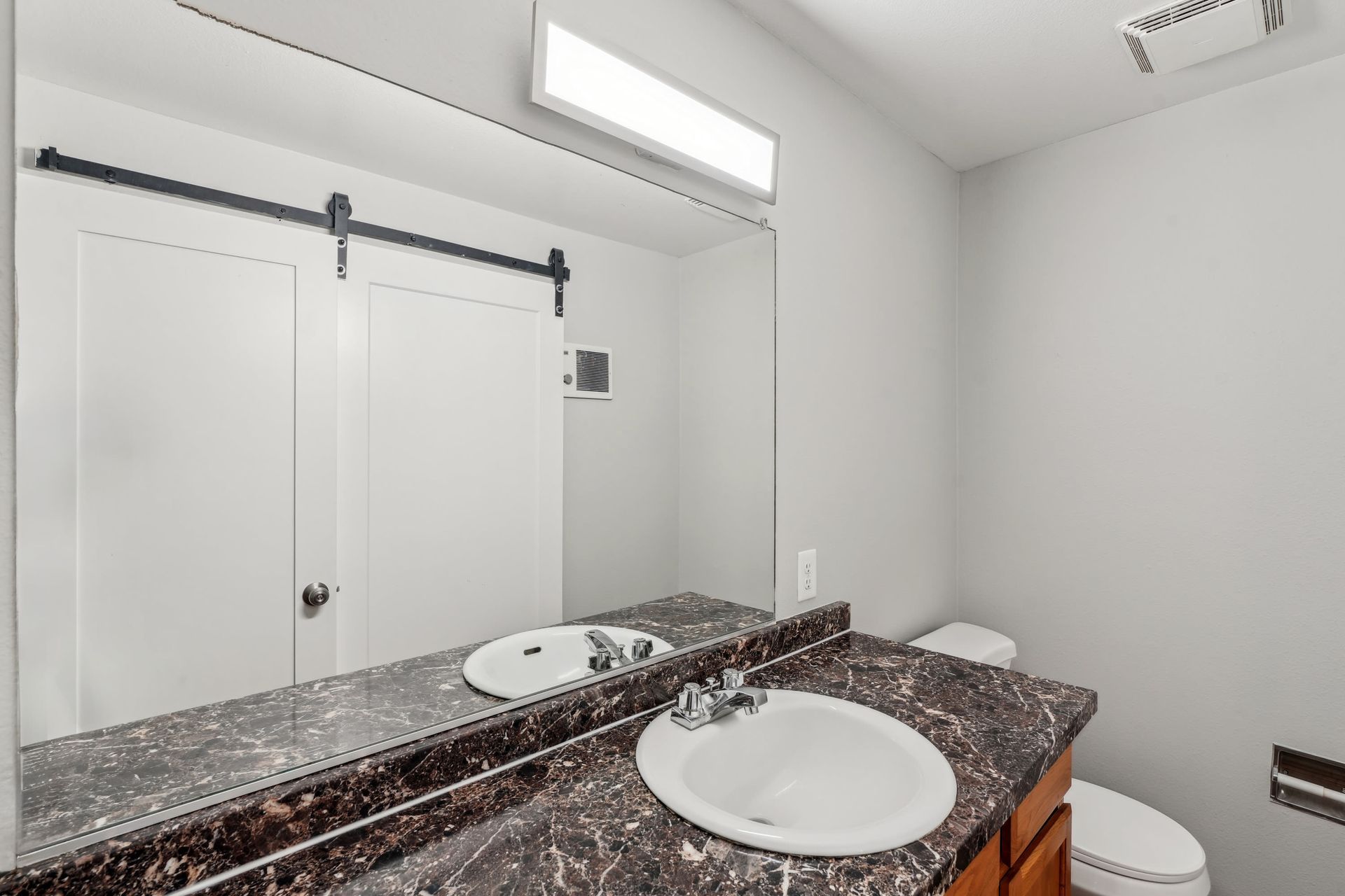 Bathroom with dark marble countertop, white sink, large mirror, and toilet.