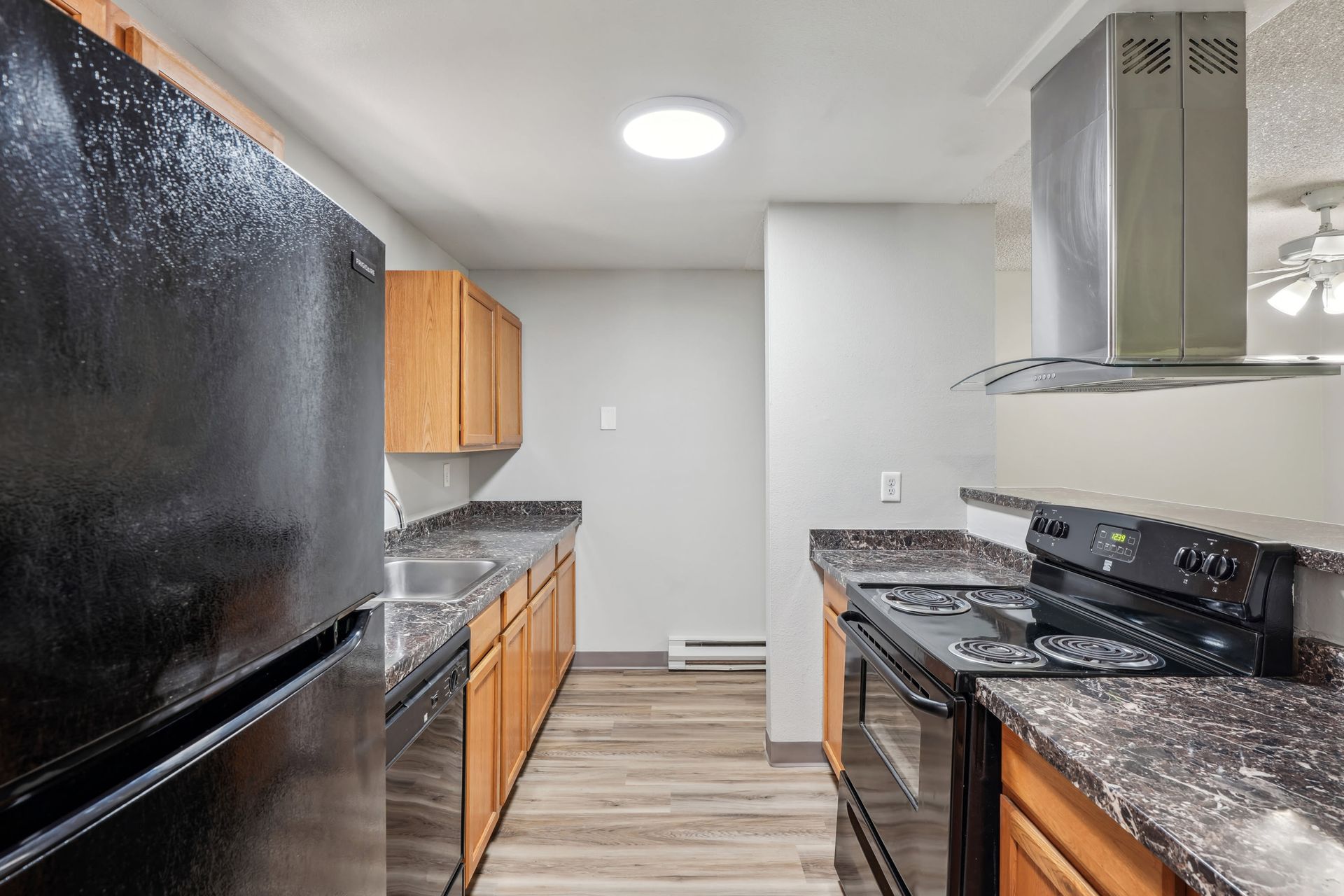 Galley-style apartment kitchen with black refrigerator, stove, and wooden cabinets.