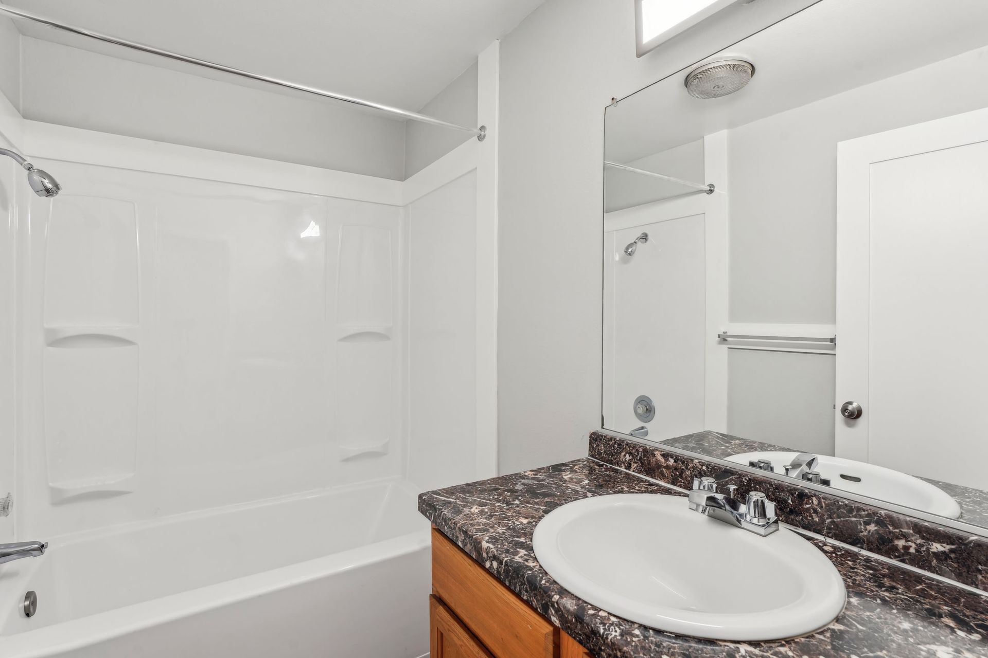 White bathroom with dark marble countertop, under-mount sink, mirror, and tub/shower.