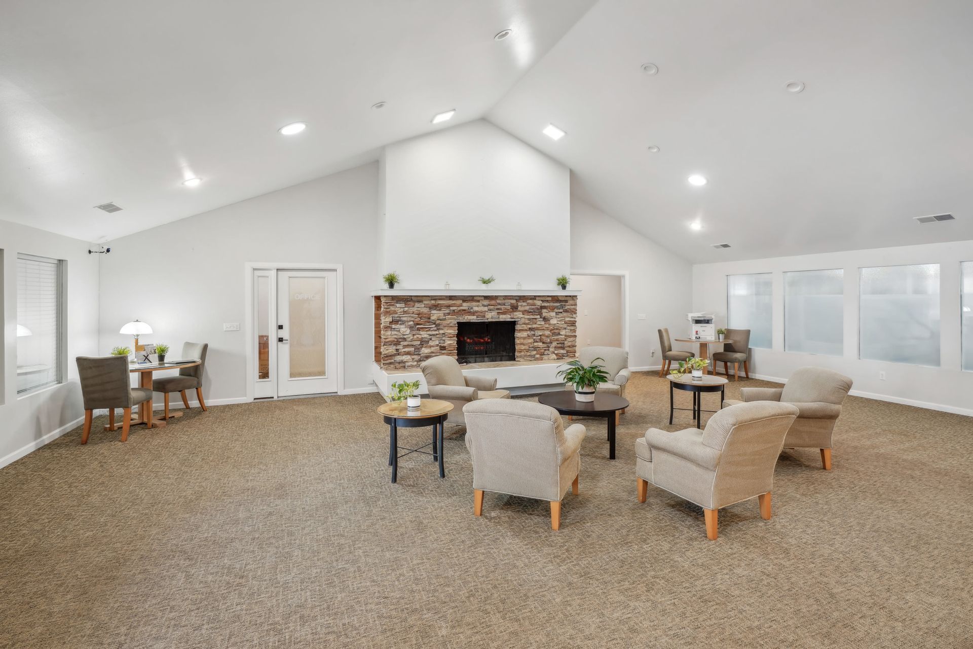 Bright community lounge with a stone fireplace and multiple seating areas.