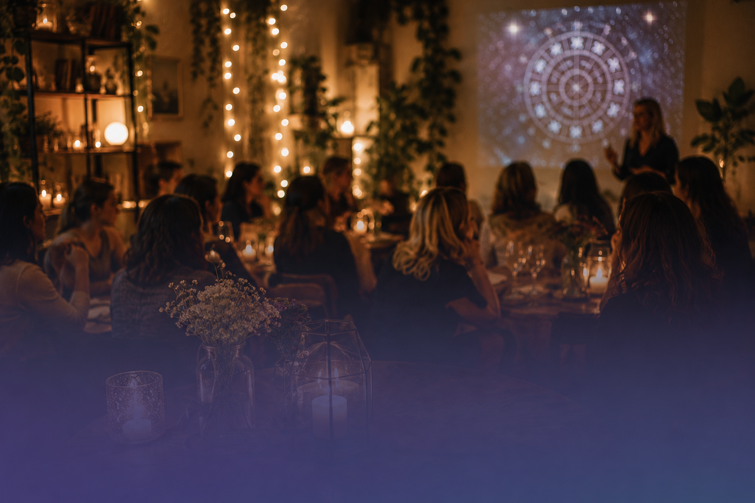 Dimly lit candlelit gathering with seated people facing a projected circular pattern on a wall.