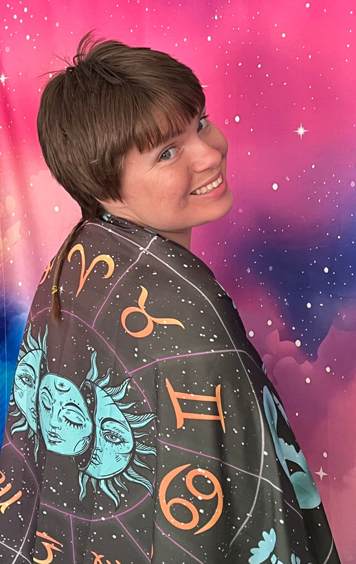 Smiling person in a dark, starry cape with zodiac symbols, turned over their shoulder on a white background
