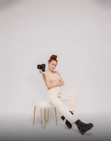A woman is sitting on a chair holding a camera.