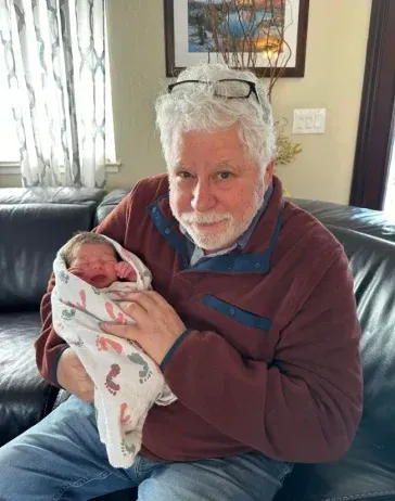 A man is holding a baby wrapped in a blanket while sitting on a couch.