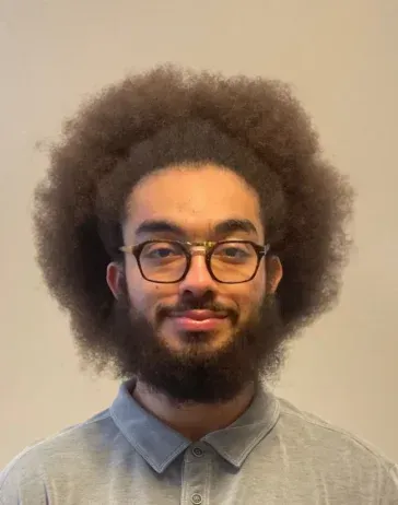 A man with an afro and a beard is wearing glasses and a gray shirt.