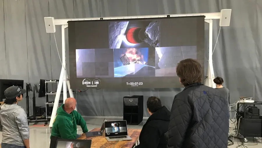 A group of people are sitting in front of a large screen.