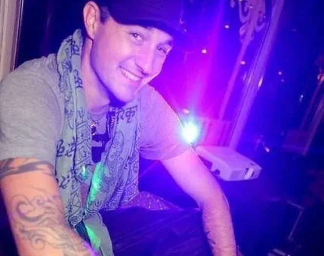 A man with a tattoo on his arm is sitting in front of a purple light.