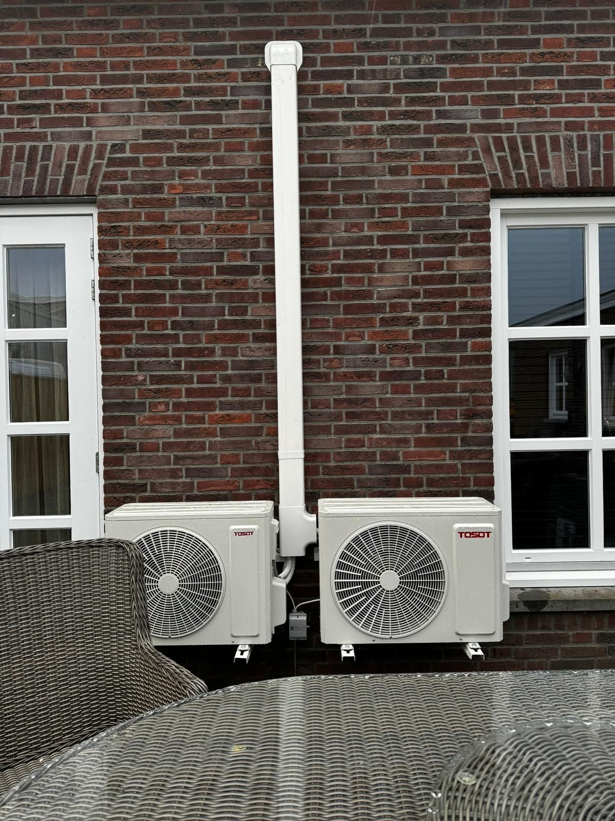 Twee mannen, gekleed in groene shirts, bekijken glimlachend tekeningen op een houten ondergrond. Een van hen heeft een gereedschapsriem om.