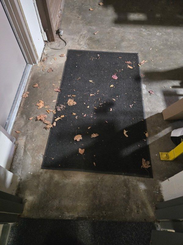 Black doormat with fallen leaves on a concrete porch near a door.