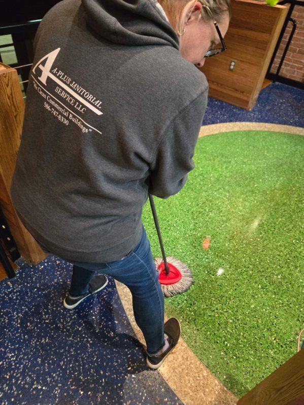 Woman playing miniature golf, aiming to hit the ball with a mop-like club on a green course.