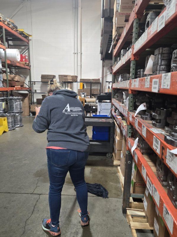 Woman in a gray hoodie and jeans in a warehouse, looking at shelves of parts.