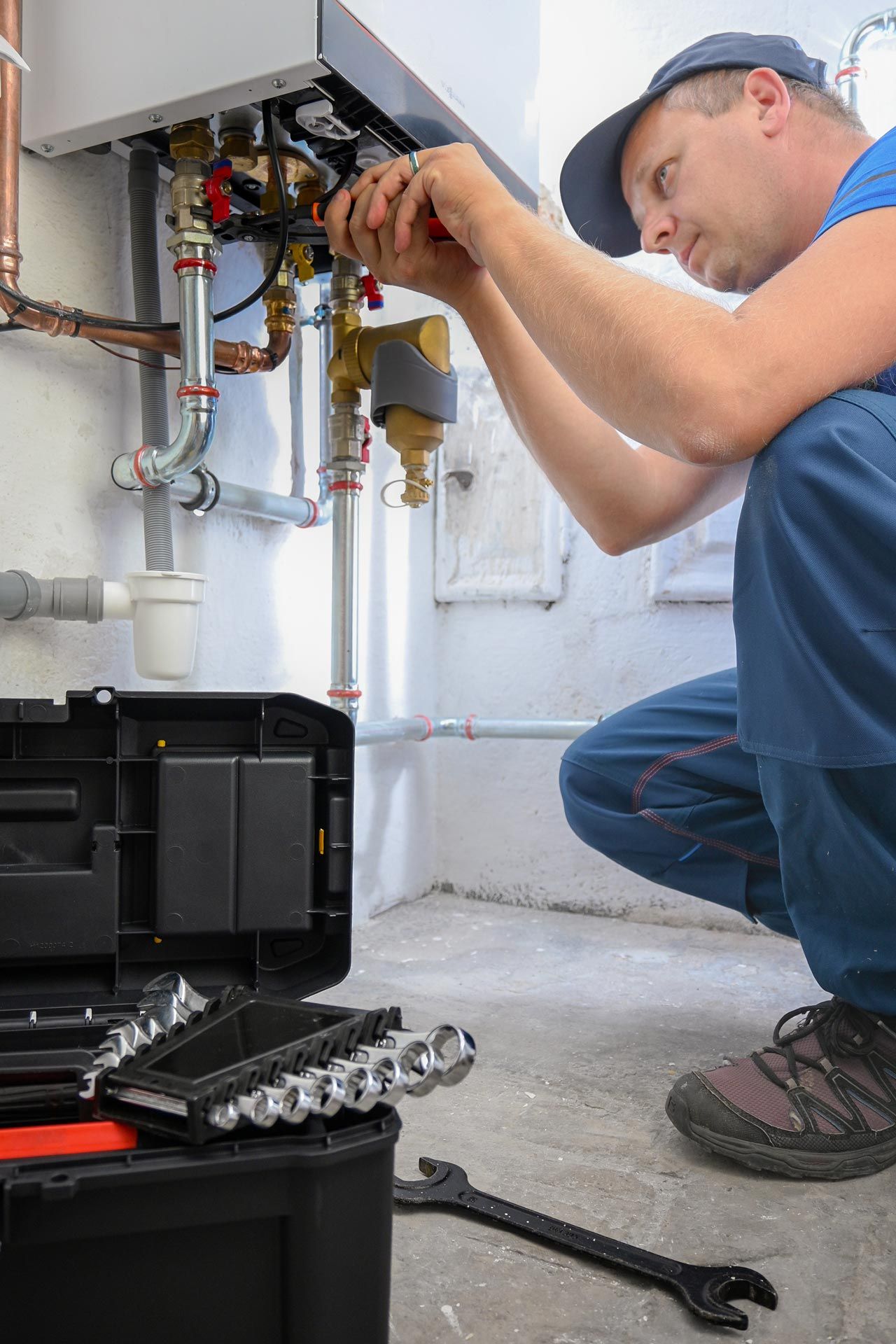 A technician wearing a blue uniform fixes heating valves while a toolbox sits close by.