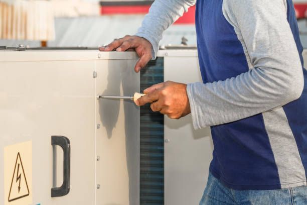 A technician using a screwdriver to repair or maintain an electrical equipment panel.
