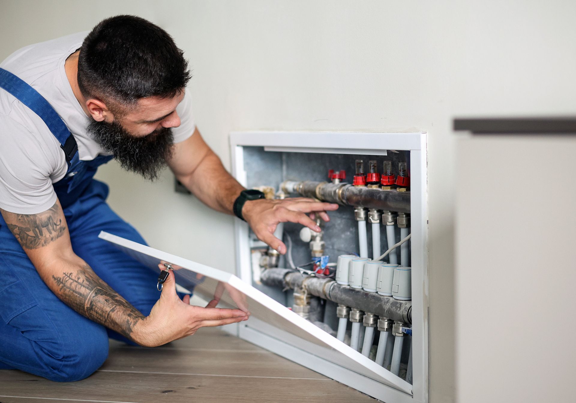 A man with a beard is fixing pipes in a room, showcasing his expertise as a heating contractor.