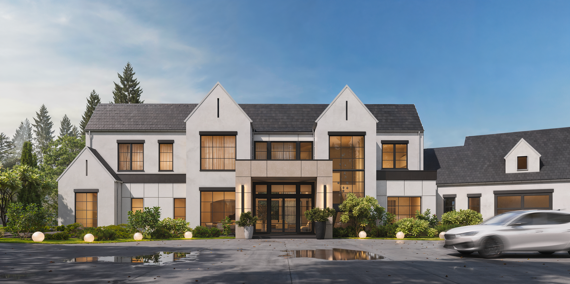 A white two-story modern farmhouse with large windows and a gray roof, set against trees under a clear blue sky.