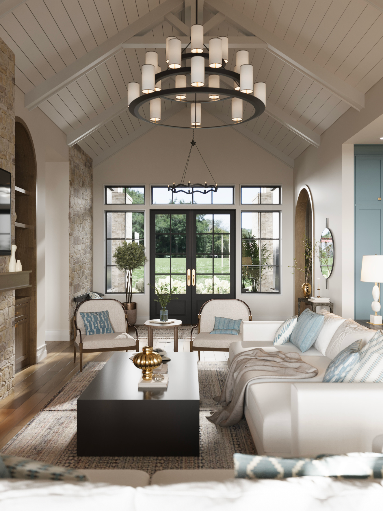 A bright living room with a vaulted ceiling, stone fireplace, large chandelier, white sofa, and French doors to a garden.