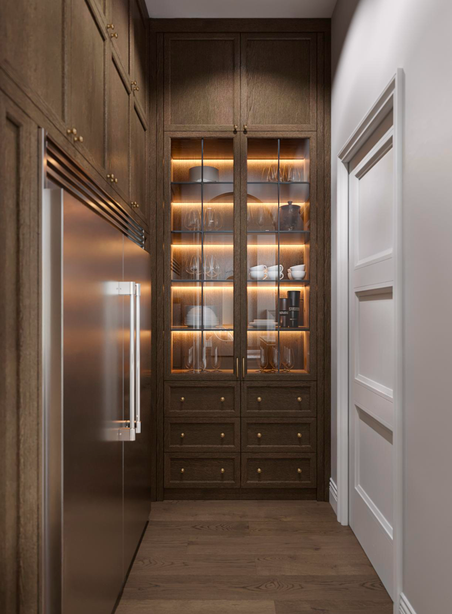 A narrow room with dark wood cabinetry, a stainless steel refrigerator, and a lit, glass-fronted display cabinet.