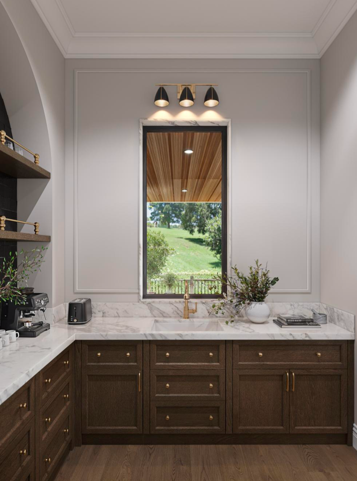A kitchen corner with dark wood cabinets, marble countertops, a window looking out at a grassy yard, and modern lighting.