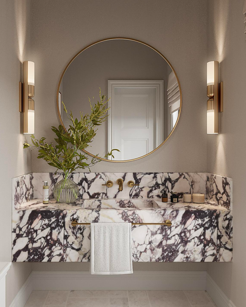 A modern bathroom vanity featuring a white marble countertop with black veining, a round mirror, and gold wall sconces.