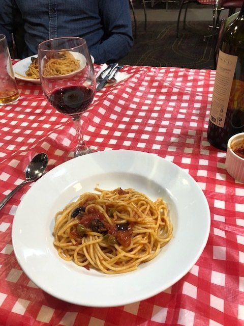 A plate of spaghetti sits on a table next to a glass of wine
