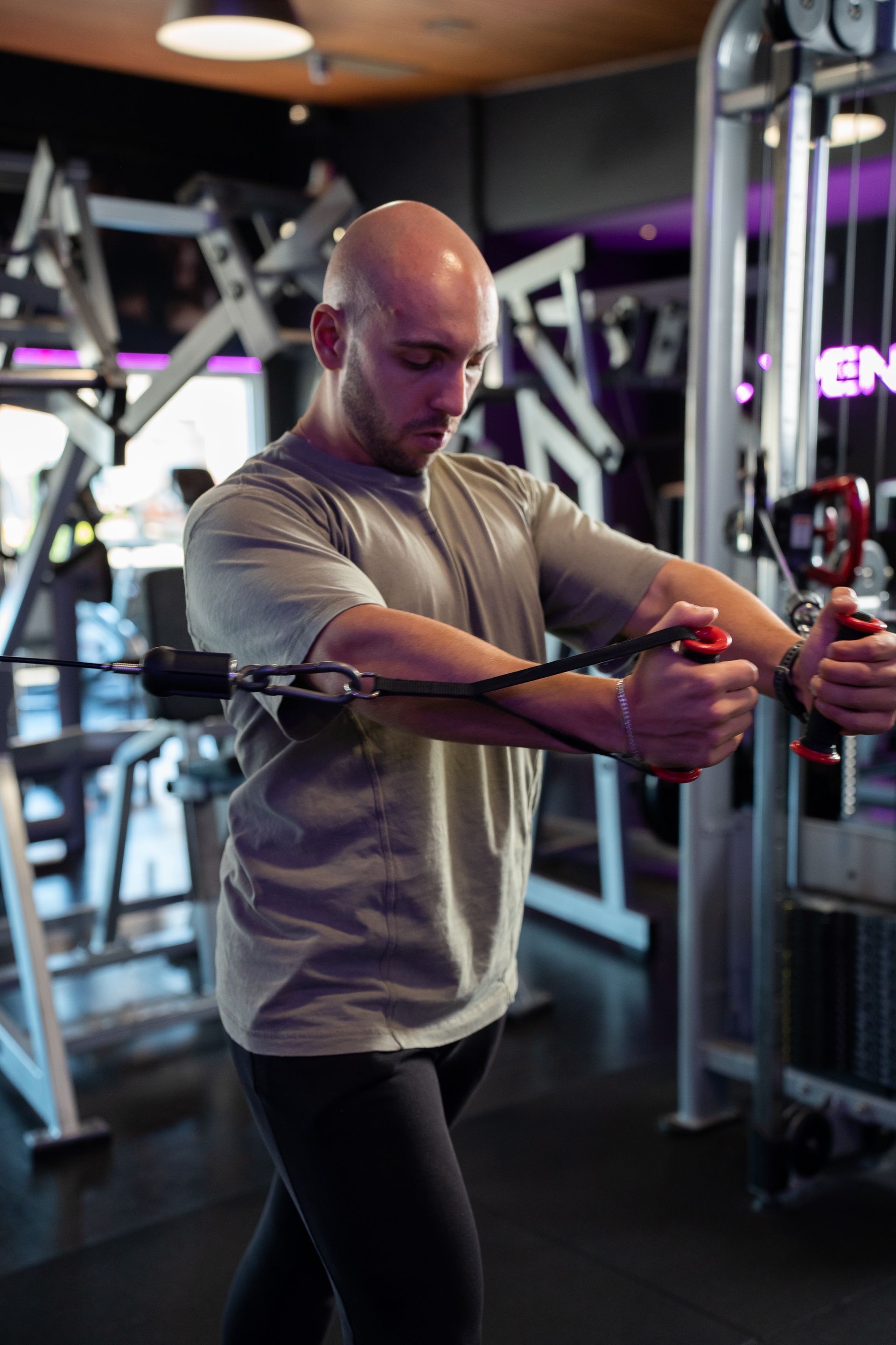 Een man, gekleed in een grijs shirt en zwarte legging, stelt een kabelmachine af in een sportschool.