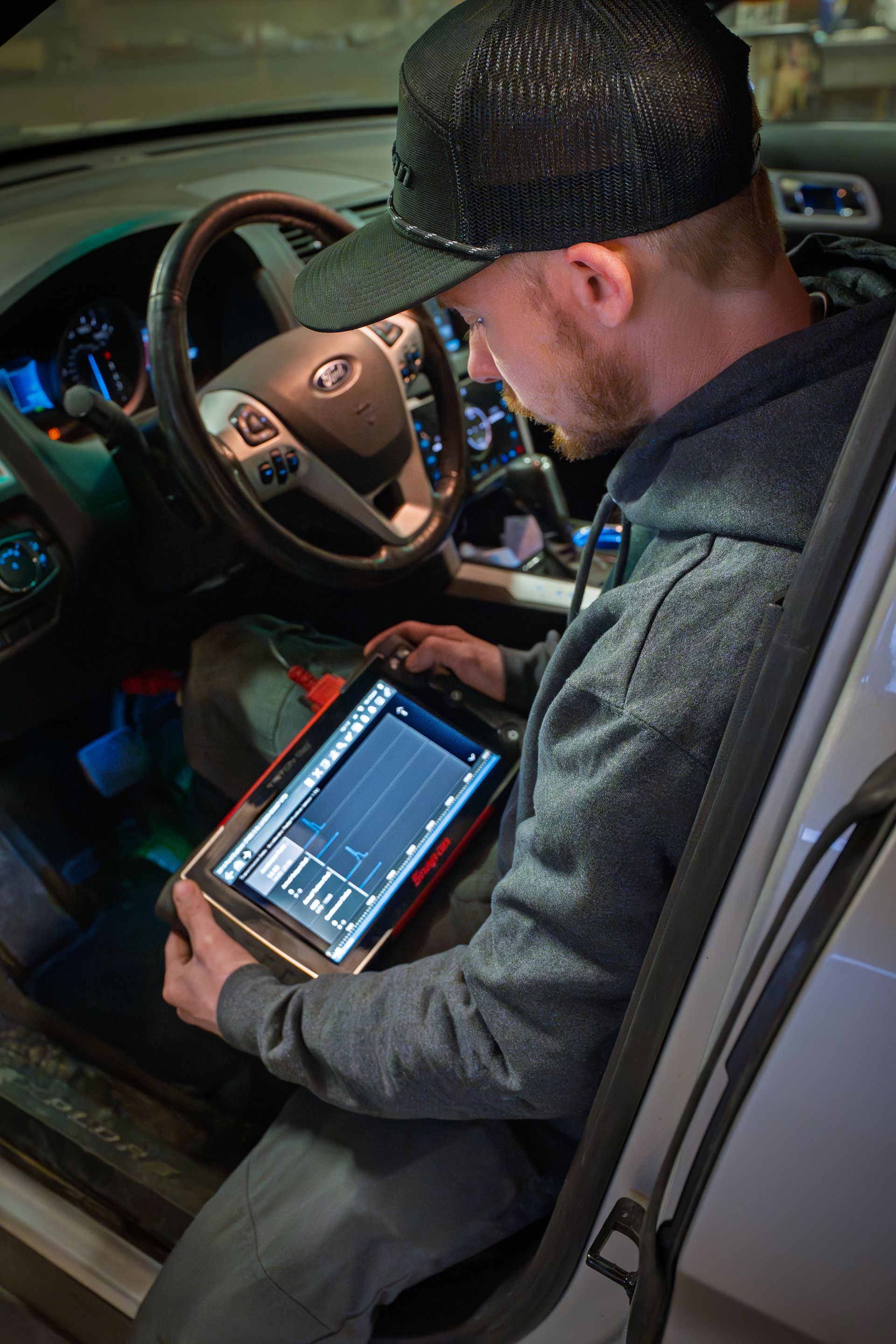 Mechanic holding a car battery, engine in the background.