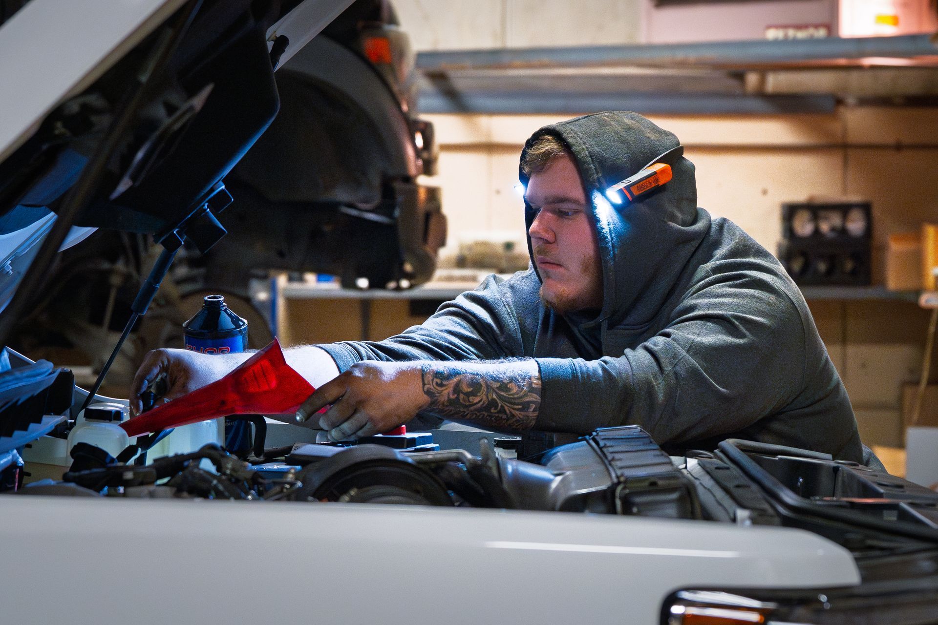 Mechanic in blue coveralls, gloves writing on a clipboard, car engine open for inspection.