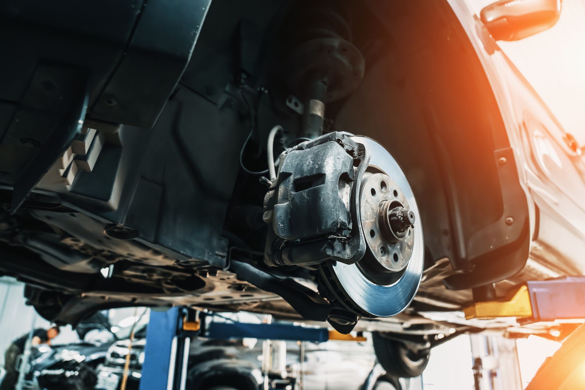 Car's front brake assembly lifted on a service lift, showing rotor, caliper, and suspension components.