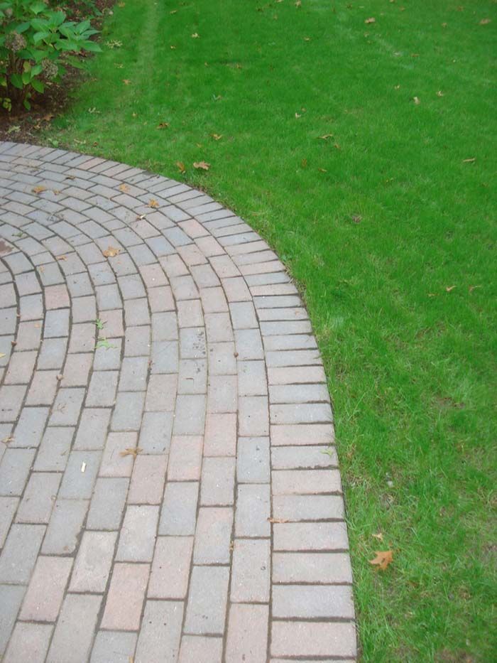 A brick walkway leading to a lush green lawn