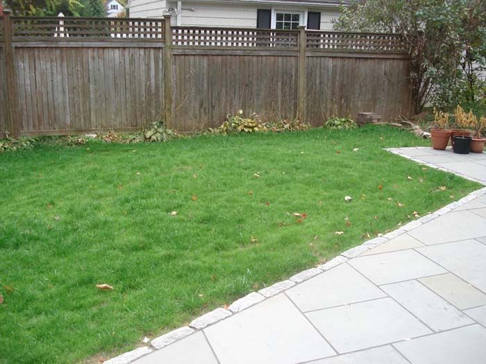 A backyard with a wooden fence and a lush green lawn