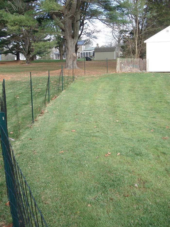 A fence surrounds a lush green field with a white house in the background.