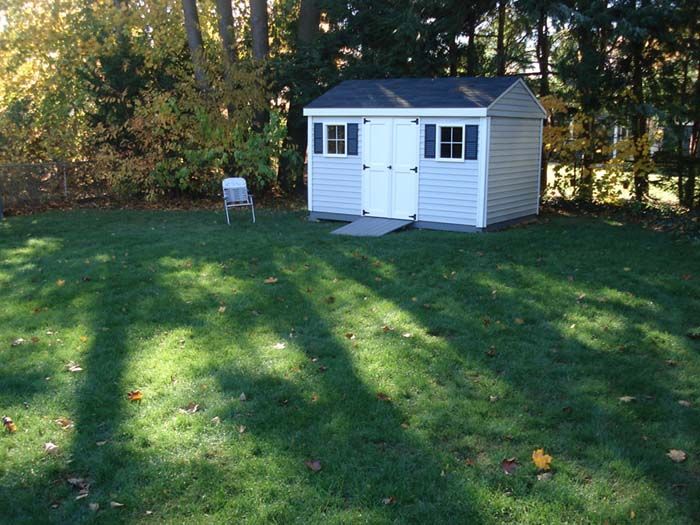 A white shed sits in the middle of a lush green yard