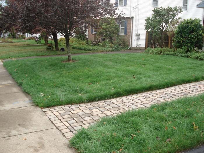 A lush green lawn with a brick walkway in front of a house