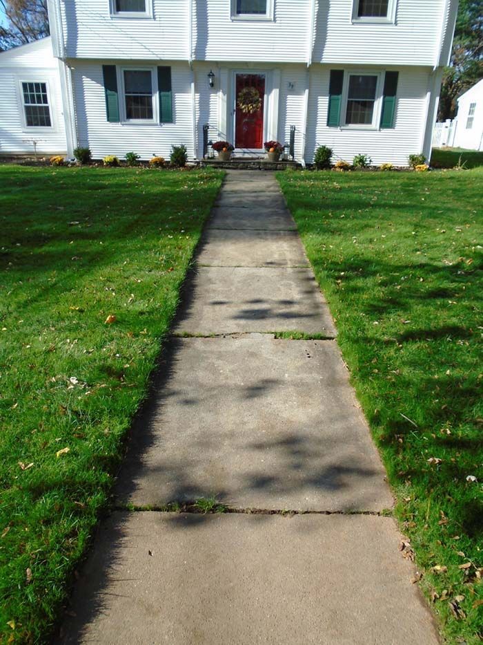 A concrete walkway leading to a white house with a red door