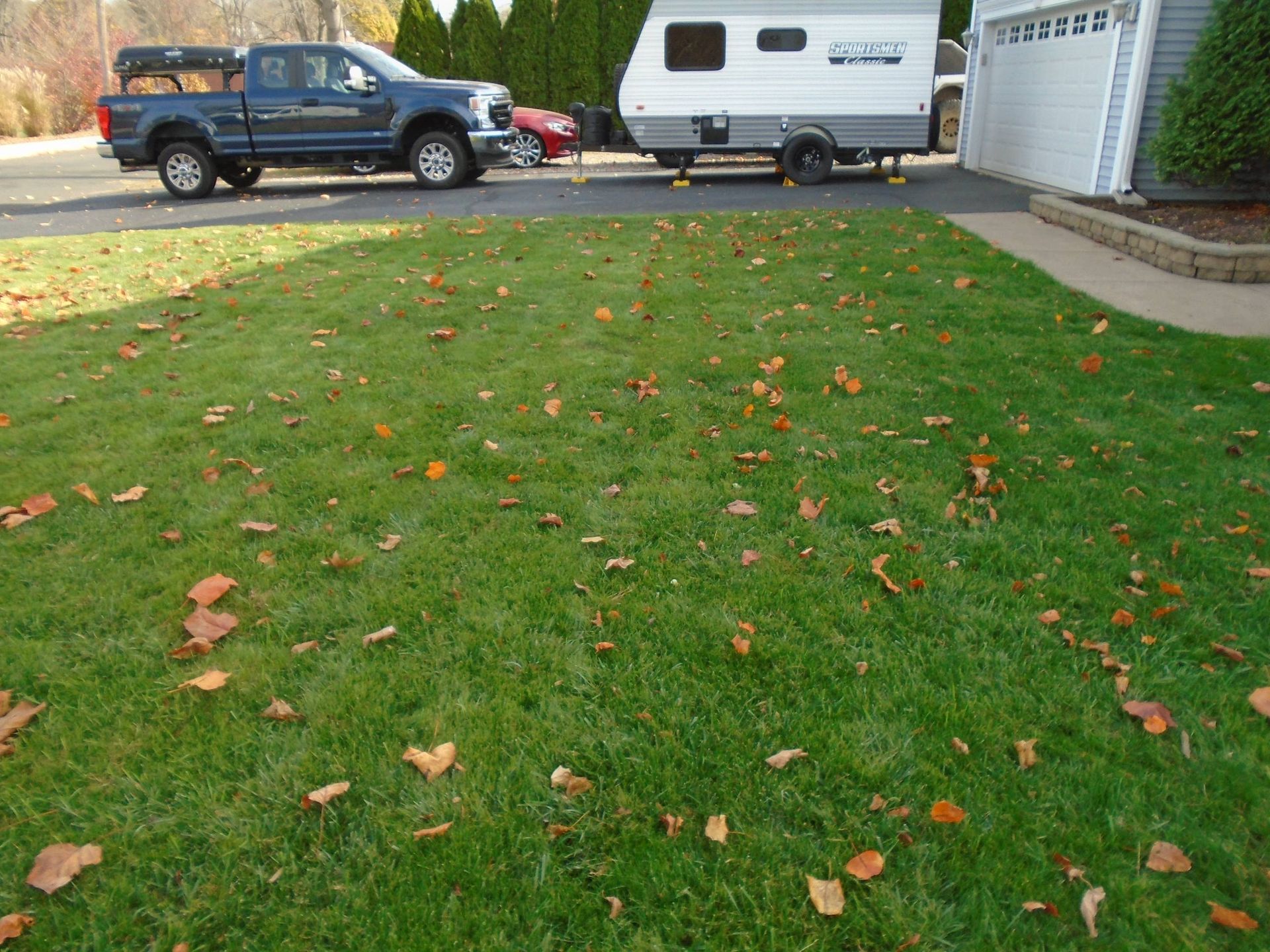 A blue truck is parked in a driveway next to a trailer.